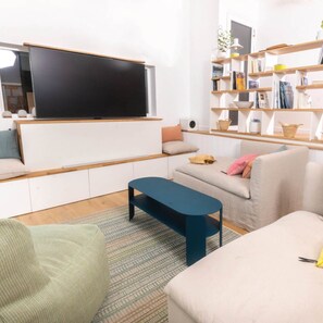 Una sala de estar moderna con un televisor de pantalla plana montado en la pared, un sofá, una mesa de centro y una estantería llena de libros y objetos decorativos.