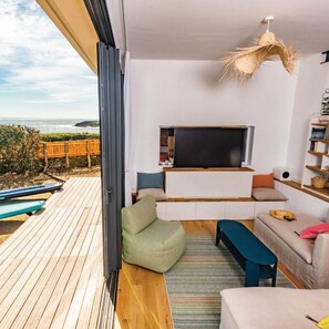 Una sala de estar moderna con televisor grande, zona de estar y vista al océano.