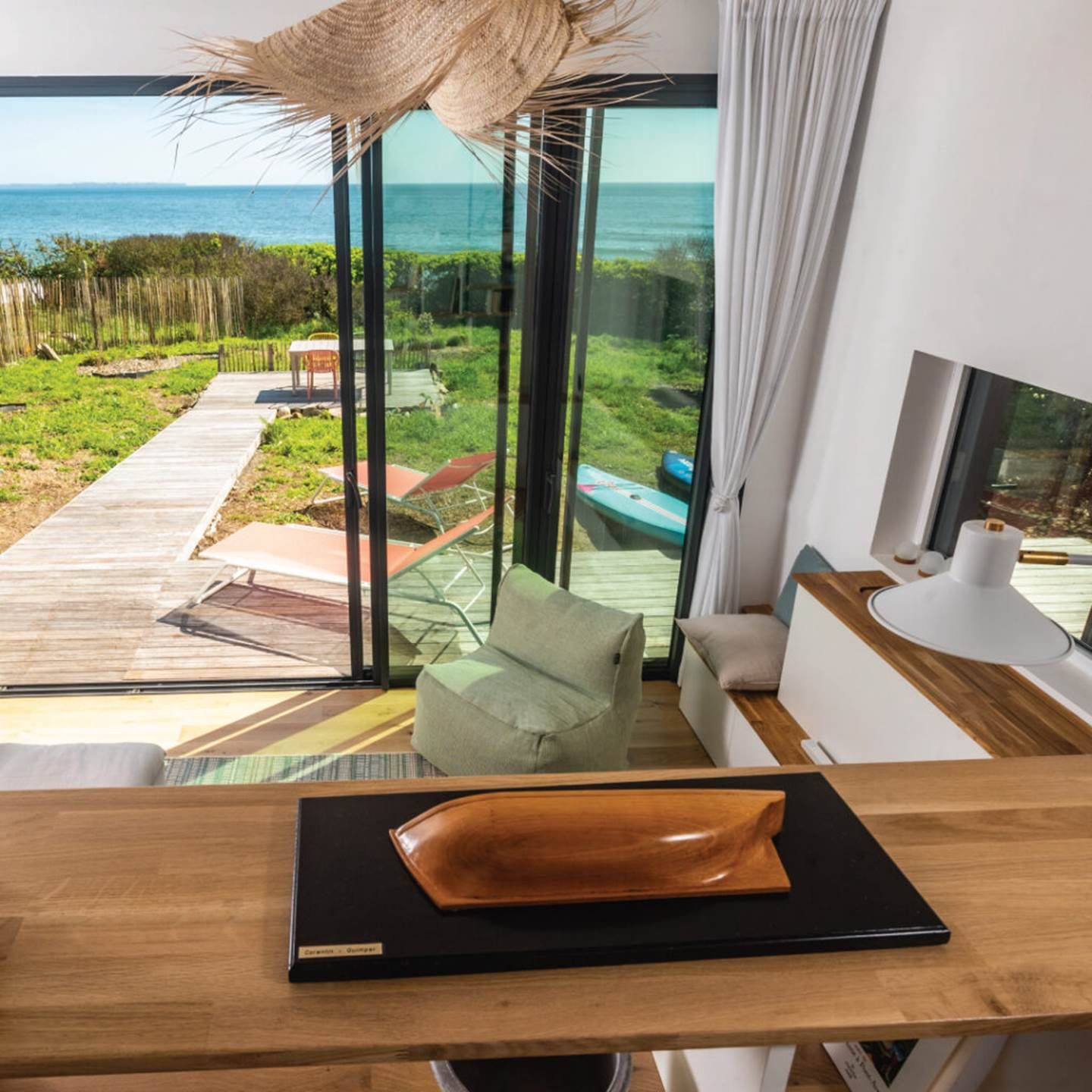 Et moderne interiør med et stort glasvindue, der giver udsigt over en have og havet.