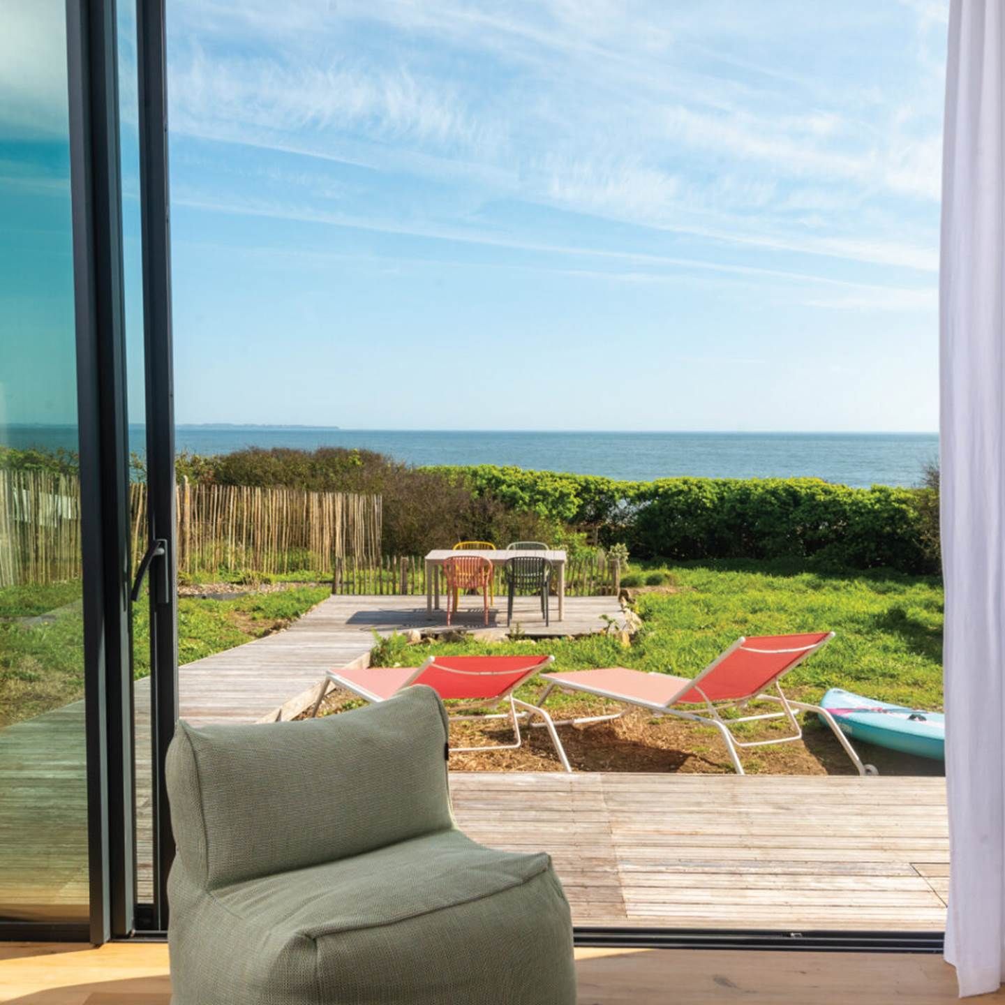A deck with a view of the sea, a chair, and a table with chairs.