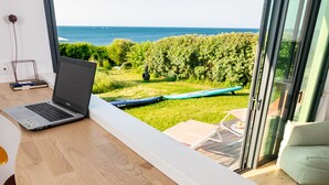 Une chambre moderne avec un bureau en bois, un ordinateur portable et une vue sur la mer grâce à de grandes fenêtres.