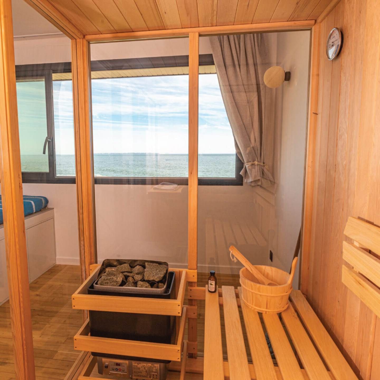 A wooden sauna room with a bench, a bucket, and a tray of stones.