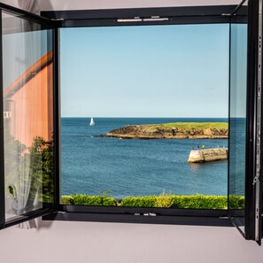 Una habitación con un ventanal grande que ofrece vistas al mar, incluyendo un velero y terreno rocoso.