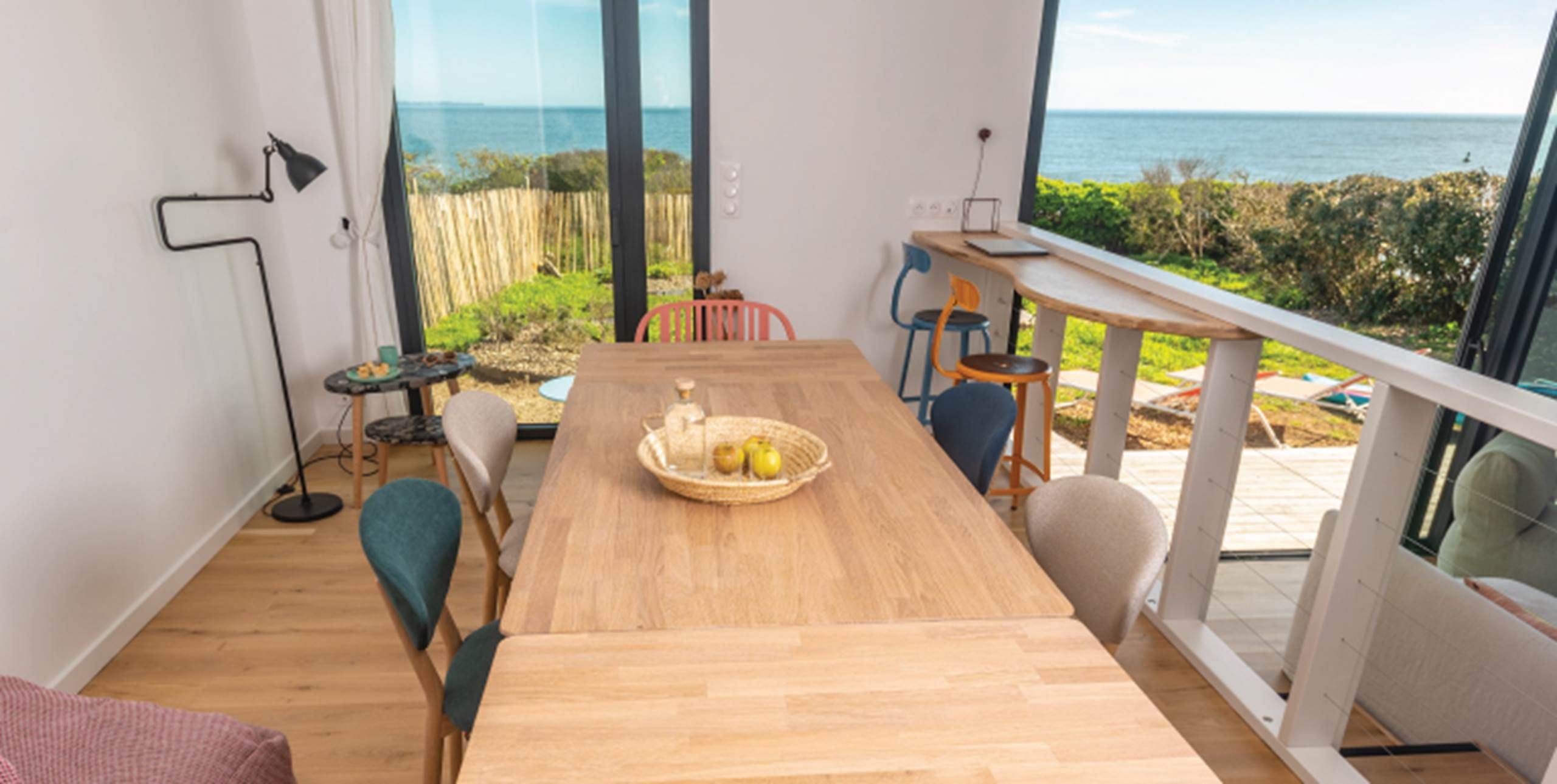 Une table à manger en bois, avec des chaises, une petite table d’appoint et une vue sur la mer.