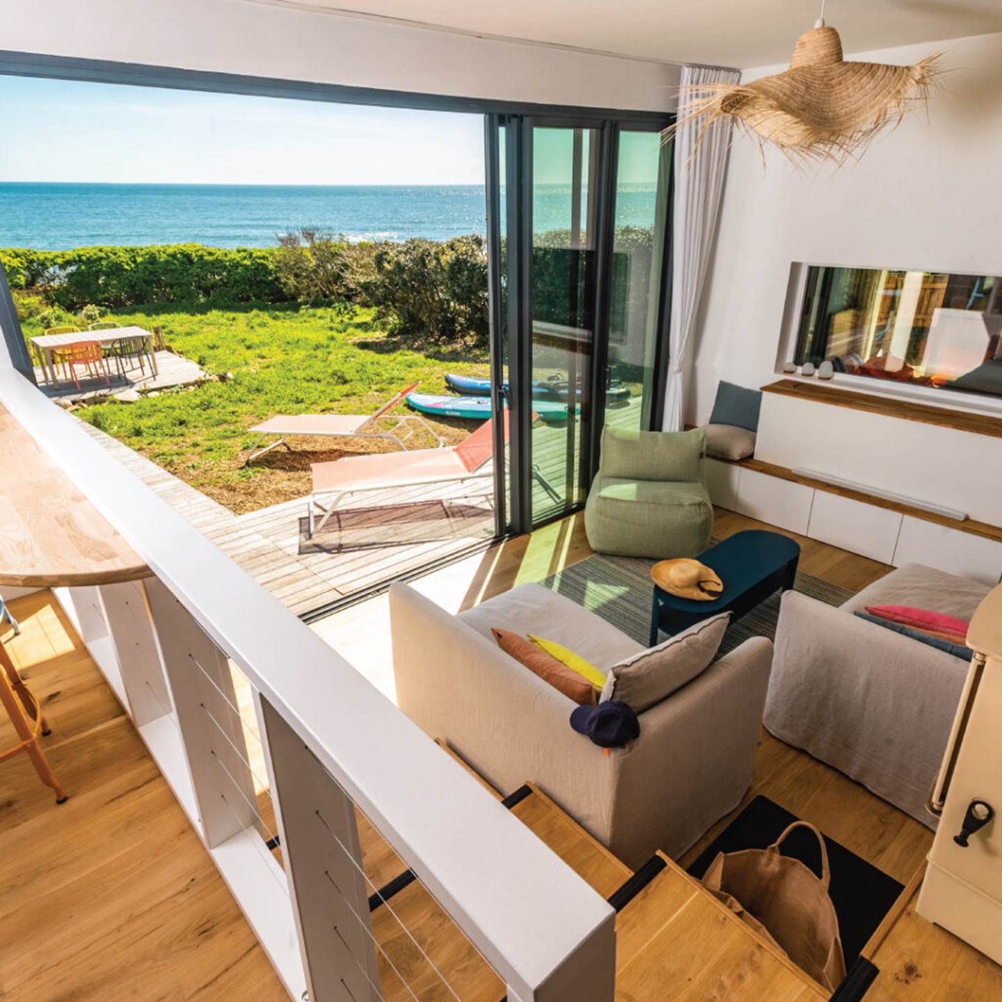 A modern interior with a balcony overlooking a grassy area and the sea.