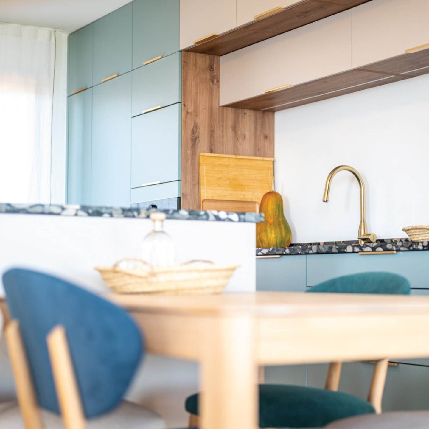 Una cocina moderna con armarios azul claro, una pared de acento de madera y una encimera negra.