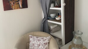 A room with a beige armchair, a painting, a wooden cabinet, and a small table with a glass pitcher. - Clean Private Bedroom,Bathroom. Private entrance. Lovely Gated Neighborhood.     (Vista)