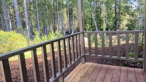 A wooden deck with a railing, surrounded by trees and a covered area.
