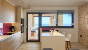 A modern kitchen with a built-in oven, microwave, and coffee maker. There is a dining area with a bench and chairs, and a view of the sea through large windows. - Lovely home in Smrika (Smrika)