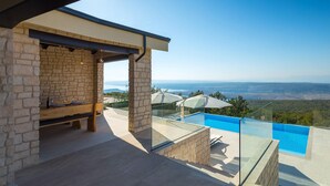 A modern outdoor seating area with stone walls and a clear view of a pool and landscape. - Lovely home in Smrika (Smrika)