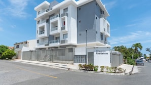 Un edificio residencial moderno de varios pisos con balcones, una entrada porticada y un cielo despejado.