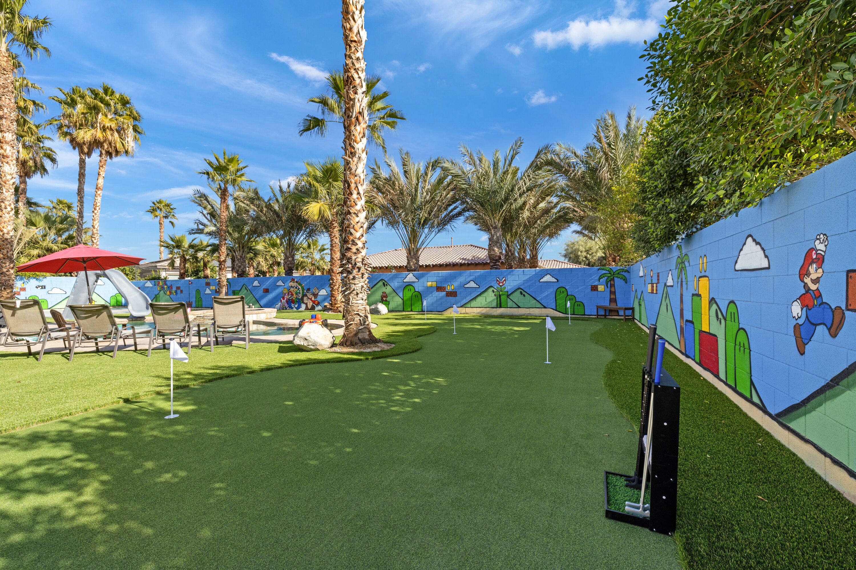 A pool area with artificial turf, palm trees, and a mural with cartoon characters.