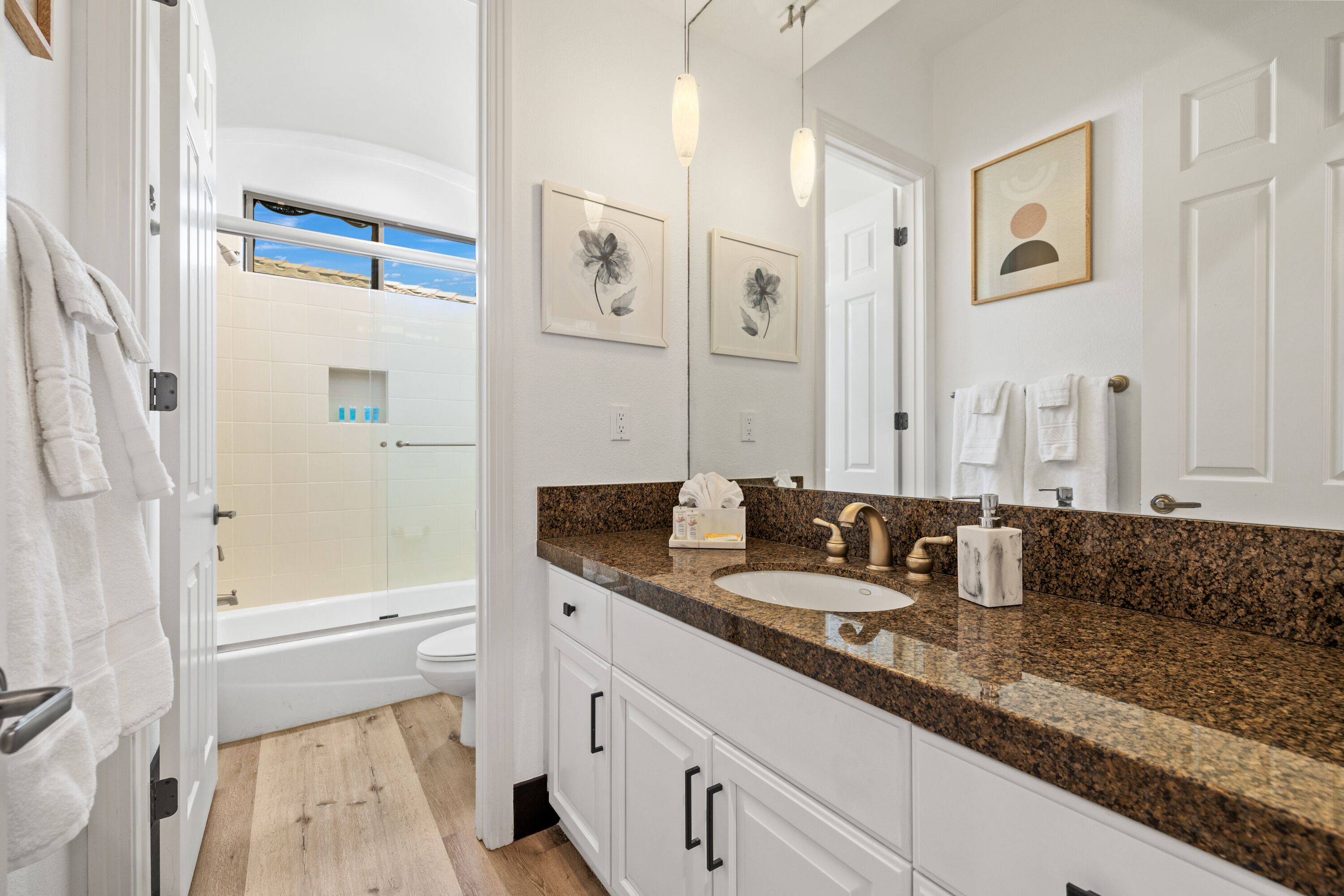 A modern bathroom with a granite countertop, white cabinets, a large mirror, and a bathtub.