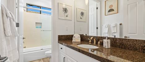 A modern bathroom with a granite countertop, white cabinets, a large mirror, and a bathtub.