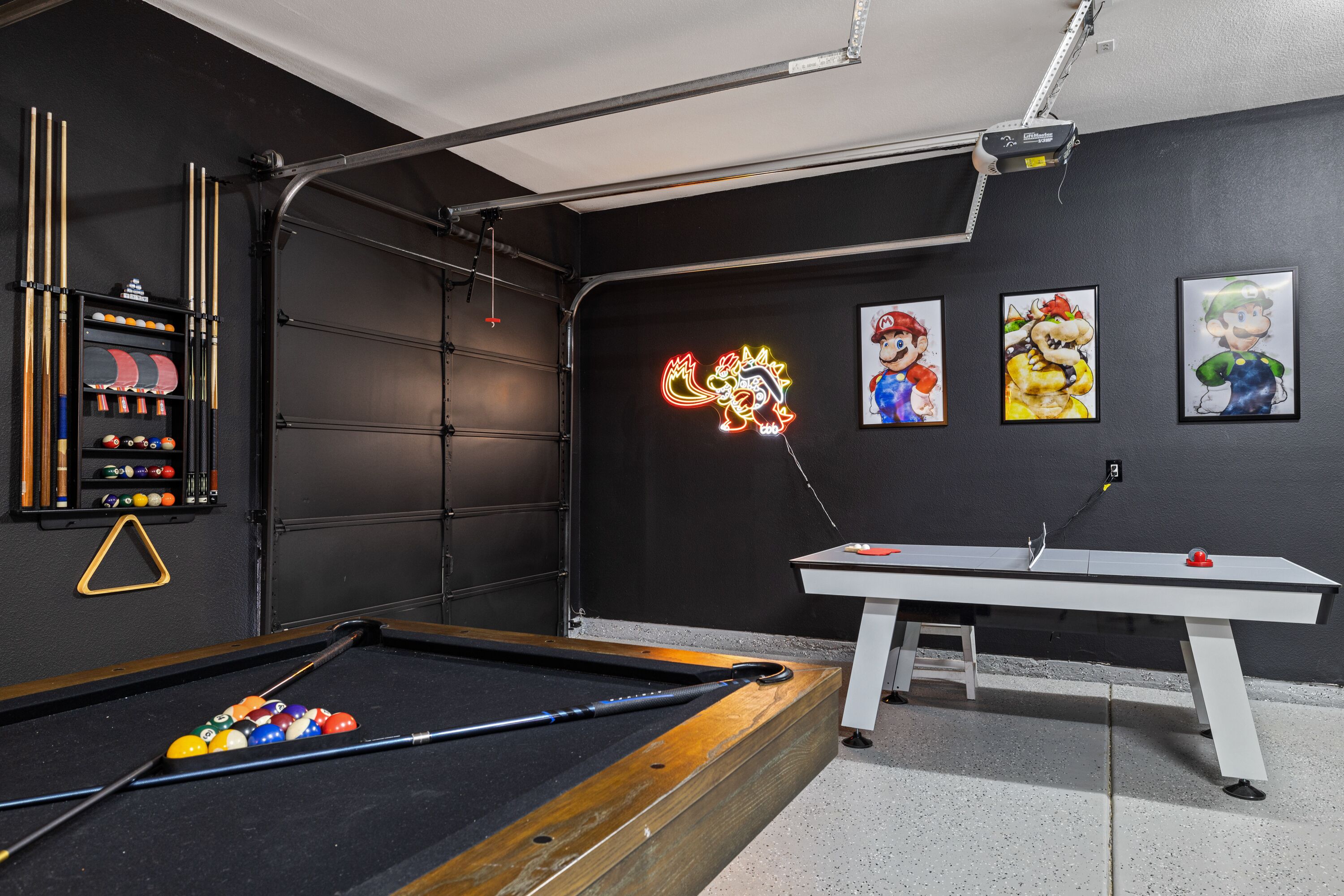 A pool table with a neon sign, a billiards rack, and Mario-themed artwork on the wall.