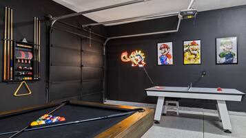 A pool table with a neon sign, a billiards rack, and Mario-themed artwork on the wall.