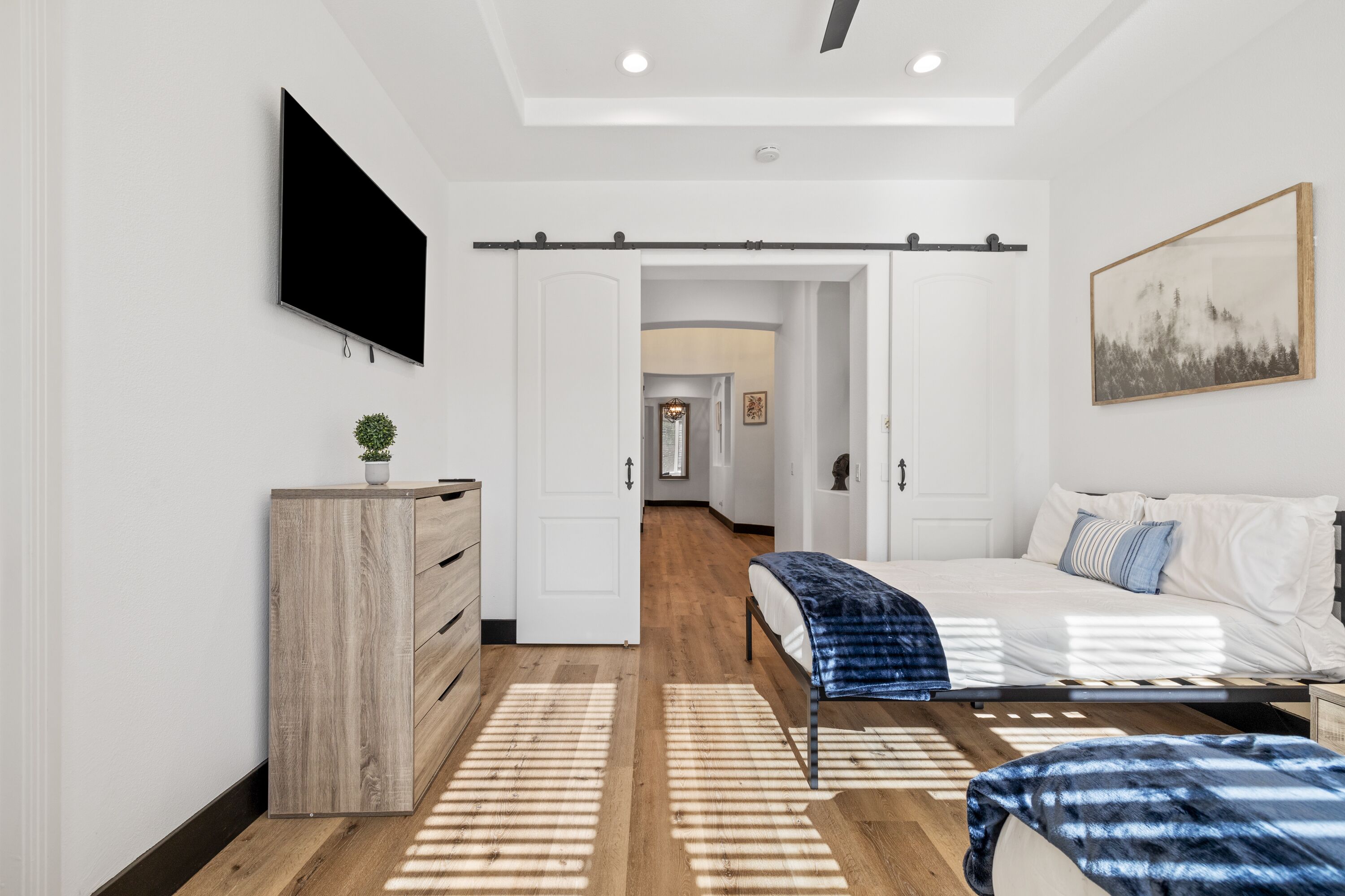 A modern bedroom with a bed, a TV, a dresser, and a hallway leading to another room.
