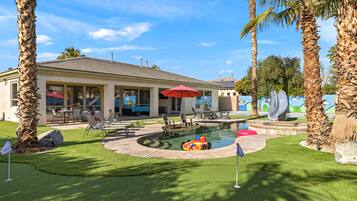 A pool area with a lounge chair, umbrella, and palm trees.