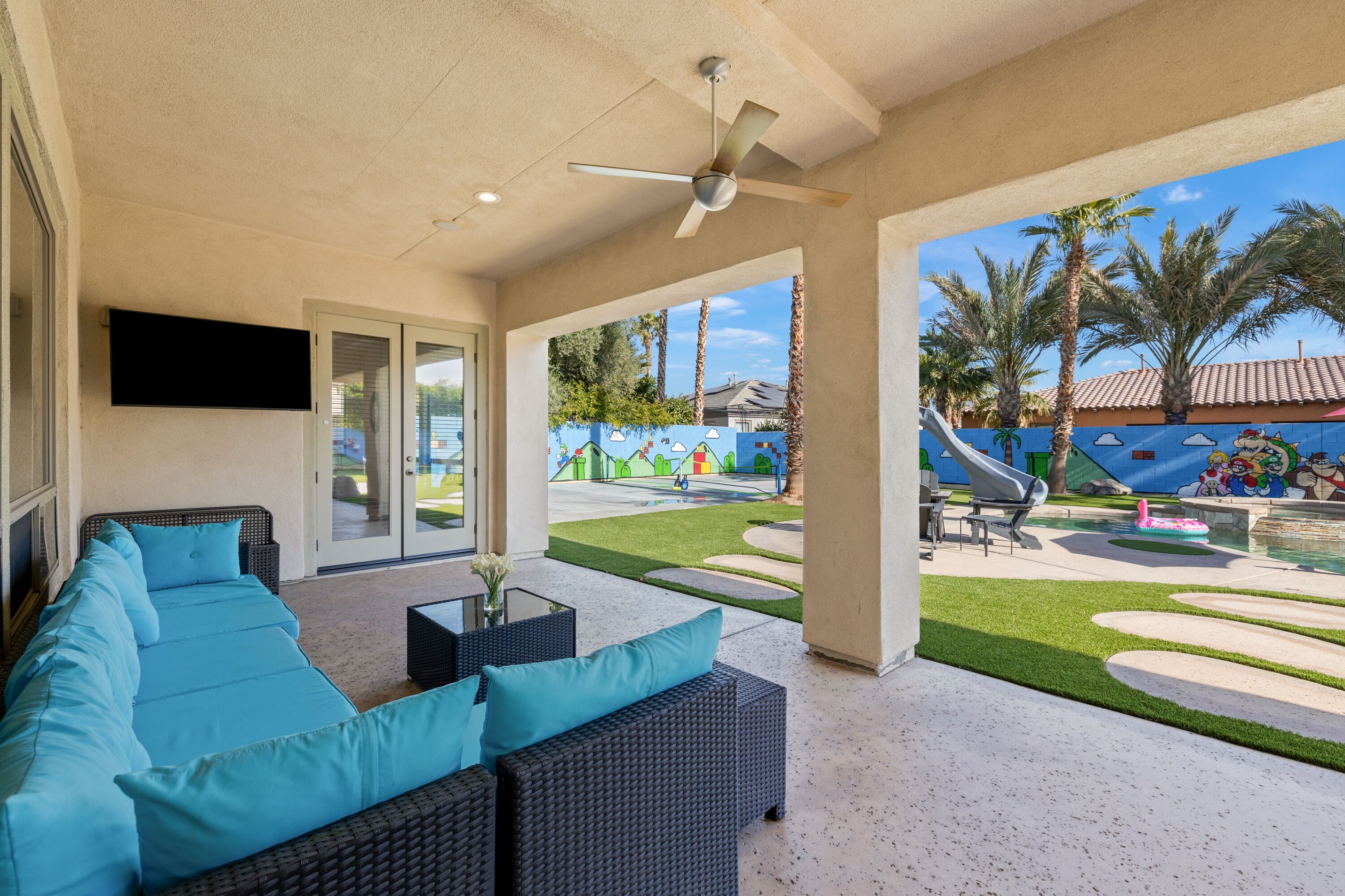 An outdoor patio with a sofa, ceiling fan, and a view of a playground and pool.