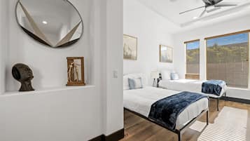 A modern bedroom with a large round mirror, two beds, a ceiling fan, and wooden flooring.