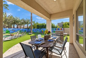 Une terrasse extérieure avec une table dressée pour les repas, un barbecue et, au fond, une piscine.