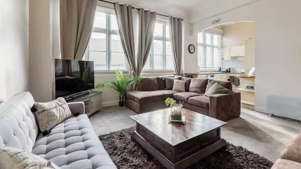 A modern living room with a sofa, a coffee table, and a TV. - The Nest - Central, Sunny & Spacious Loft (Te Aro)