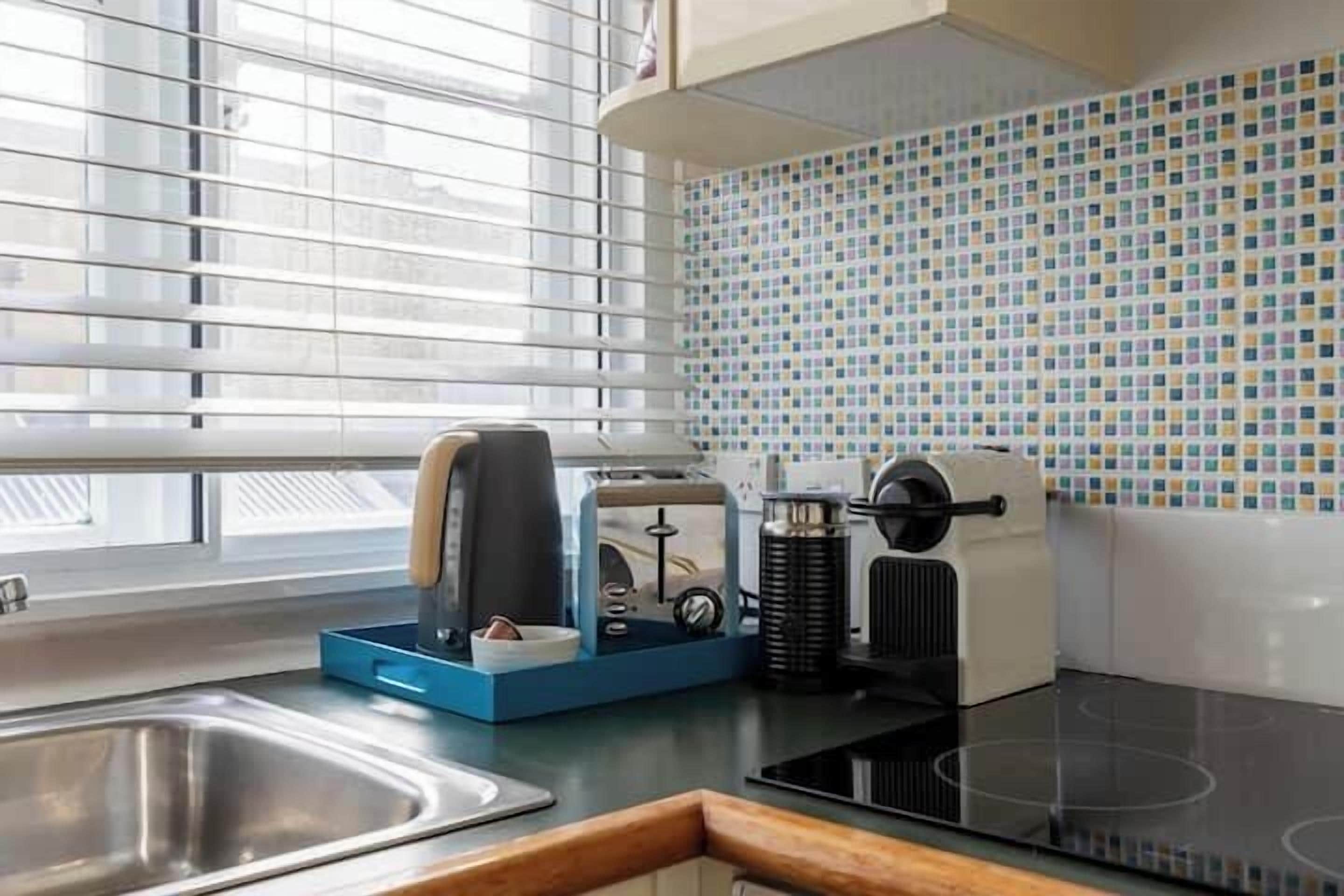 A modern kitchen with a stainless steel sink, a black induction cooktop, and a blue appliance on the counter.