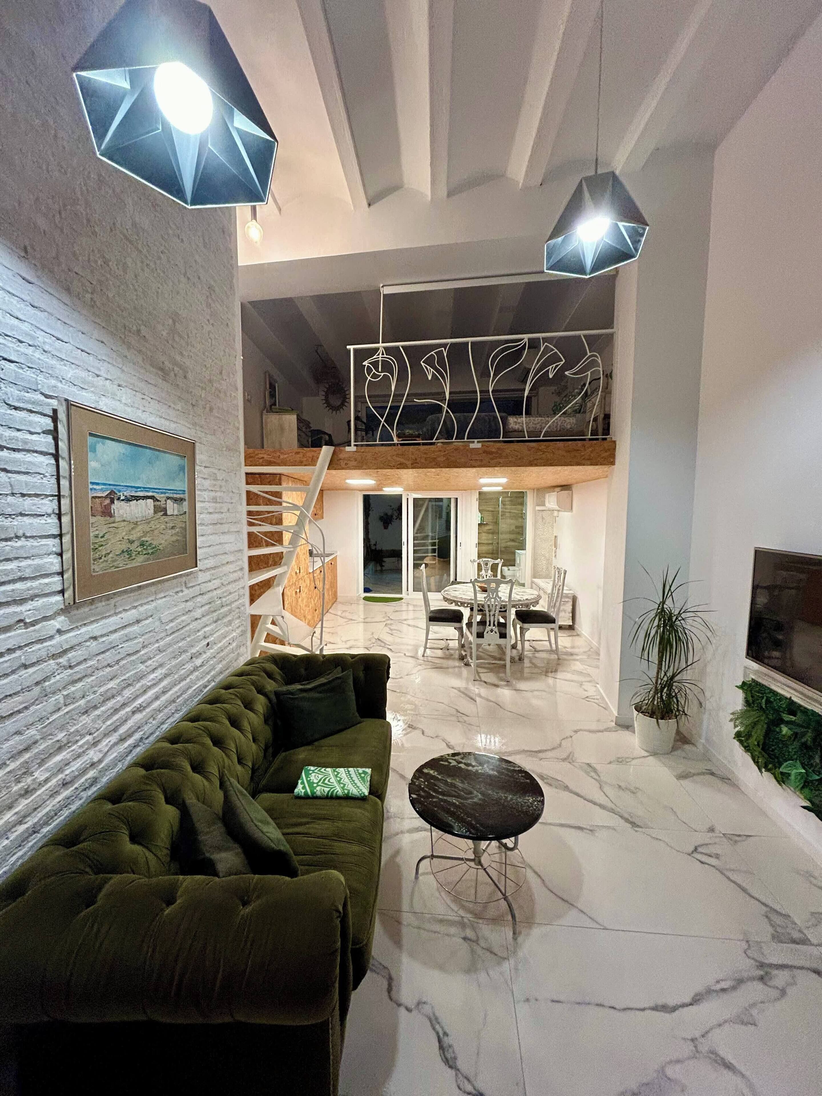 A modern living room with a green sofa, a marble floor, and a dining area with a table and chairs.
