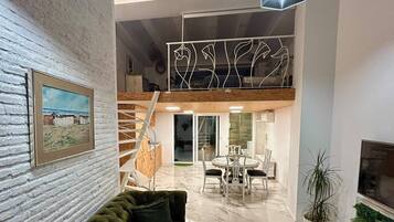 A modern living room with a green sofa, a marble floor, and a dining area with a table and chairs.