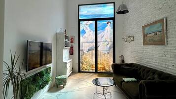 A modern living room with a large TV, a sofa, a coffee table, and a view through a glass door.