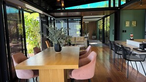 A modern dining area with a wooden table and pink chairs, surrounded by large windows offering a view of greenery. - Beautiful Finca with Jacuzzi. Large green areas, surrounded by vegetation. (Rionegro)