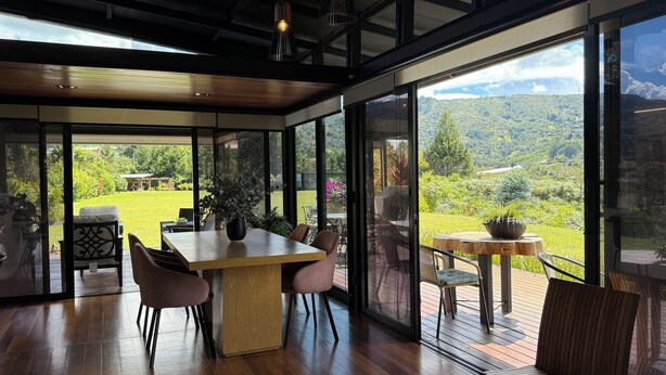 A modern interior with a wooden dining table, chairs, and a view of a lush garden and hills. - Beautiful Finca with Jacuzzi. Large green areas, surrounded by vegetation. (Rionegro)