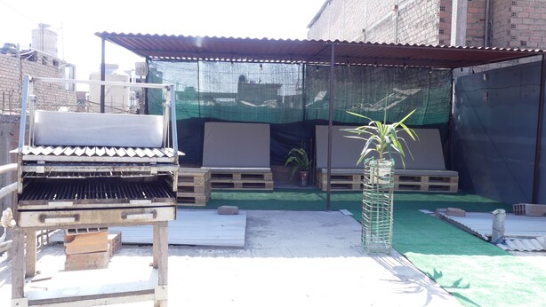 A covered outdoor area with a barbecue grill, wooden benches, and a small potted plant. - El Tip Viajero, Apartaments and Coworking  Lima Perú (San Martín de Porres)