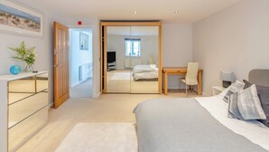 A modern bedroom with a bed, bedside table, and a desk with a chair. There is a mirror, a globe, and a plant on the dresser. - 2 bedroom accommodation in Torquay (Torquay)