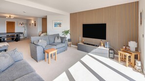 A modern living room with a grey sofa, a wooden coffee table, a flat-screen TV mounted on a striped wall, and a ceiling fan. - 2 bedroom accommodation in Torquay (Torquay)