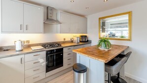 A modern kitchen with white cabinets, a stainless steel range, a built-in oven, a coffee maker, and a bar stool. - 2 bedroom accommodation in Torquay (Torquay)