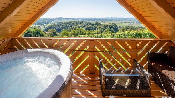 Ein Whirlpool auf einer Holzterrasse mit Blick auf eine grüne Landschaft.