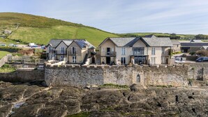 Un hotel costero con paredes de piedra, edificios de varios pisos y vistas al mar.
