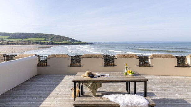 Una terraza de madera con una mesa lista para dos, con vista a una playa y al océano.