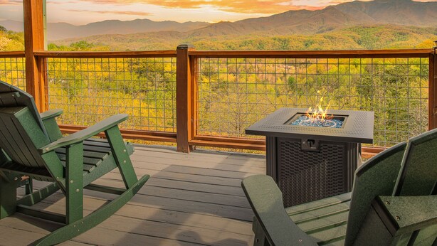 Terraza con sillones mecedores verdes y una chimenea, con vistas a un paisaje montañoso.