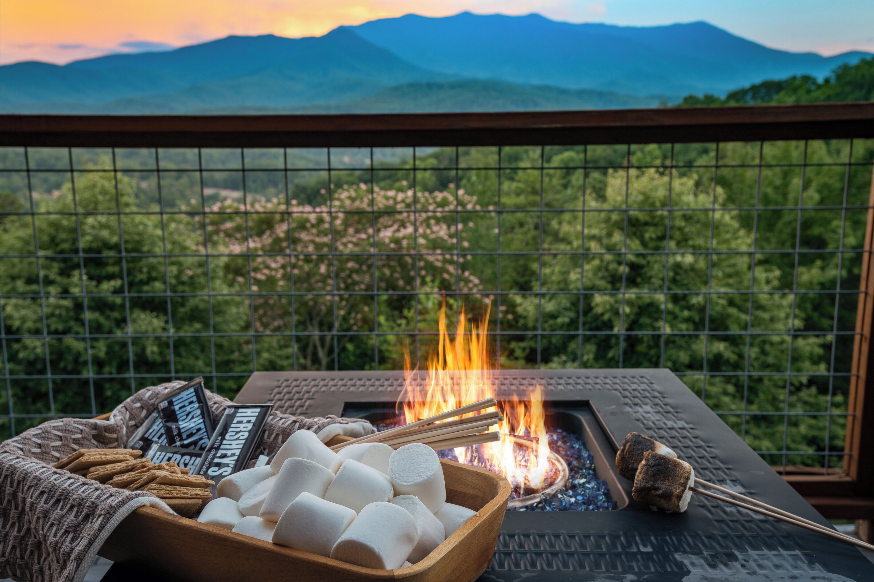 A fire pit with marshmallows and a magazine, overlooking a mountainous landscape.