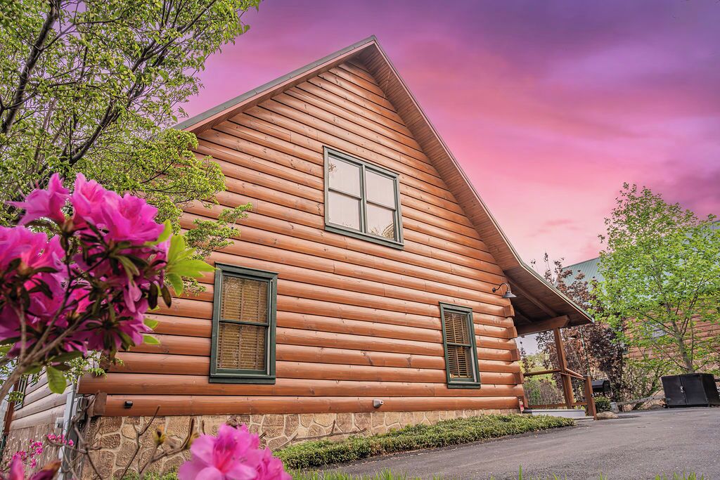A log cabin with a stone foundation, two windows with shutters, and a porch.