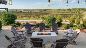 An outdoor seating area with Adirondack chairs and a fire pit, overlooking a vineyard. - Tuscan Style Wine Country Getaway (Paso Robles)