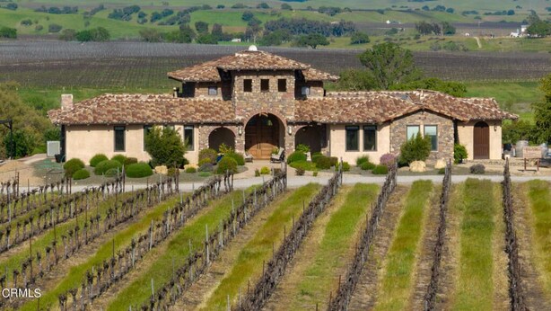A large, rustic building with a tiled roof and multiple arches, surrounded by vineyard rows. - Tuscan Style Wine Country Getaway (Paso Robles)