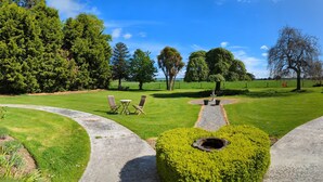 A well-maintained park with a central circular path, benches, and a fountain. - Mainholm Lodge (Pomahaka)