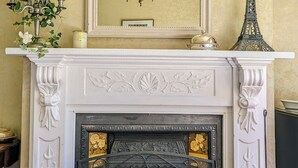 A fireplace with intricate white carvings, a large mirror above it, and a chandelier hanging from the ceiling. - Mainholm Lodge (Pomahaka)