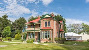 A two-story brick house with a red roof and green trim, surrounded by a well-maintained lawn and trees. - Mainholm Lodge (Pomahaka)