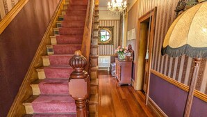 A grand staircase with a wooden handrail and carpeted steps, leading to a landing with a chandelier and a mirror. - Mainholm Lodge (Pomahaka)