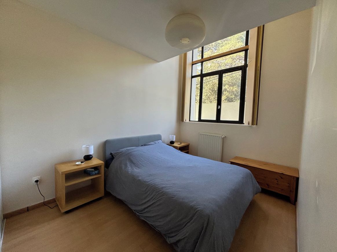 A bedroom with a bed, bedside tables, a window, and a radiator.
