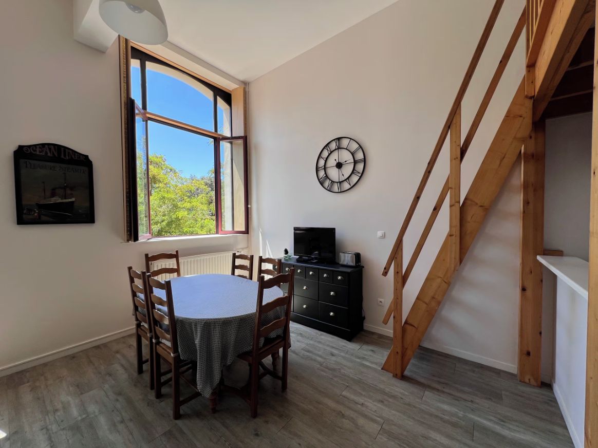 A dining area with a table and chairs, a clock on the wall, and a staircase.